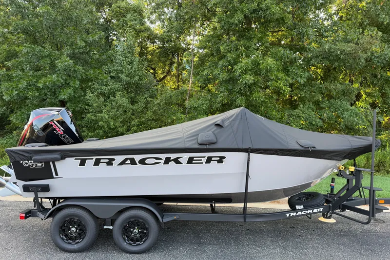 Slide: The Image of 2027 Tracker Targa V-18 Combo boat on trailer, covered, parked near lush greenery. - 20