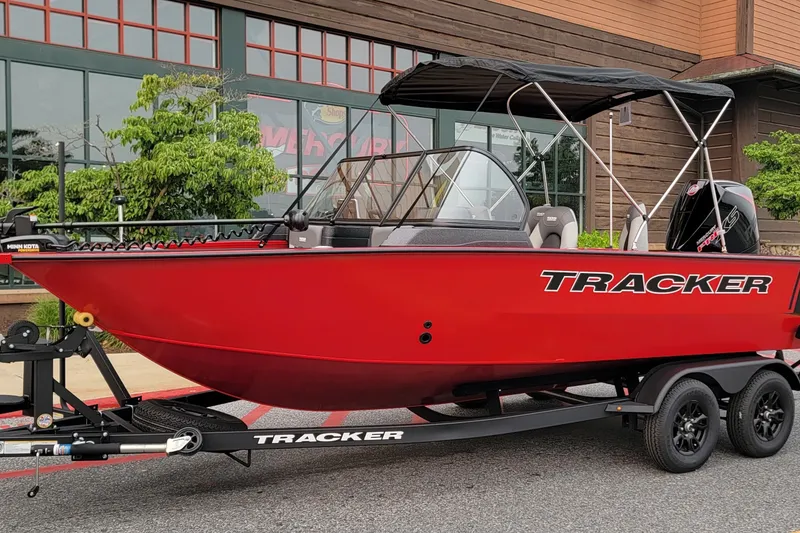 The Image of Red 2027 Tracker Targa V-18 Combo boat on trailer, parked outside a building. - 0