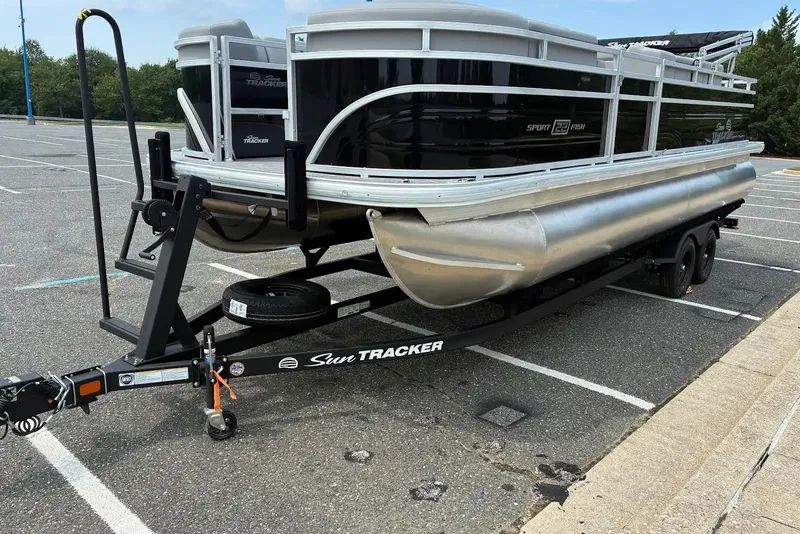 The Image of 2027 Sun Tracker SportFish 22 DLX pontoon boat on trailer in parking lot. - 0