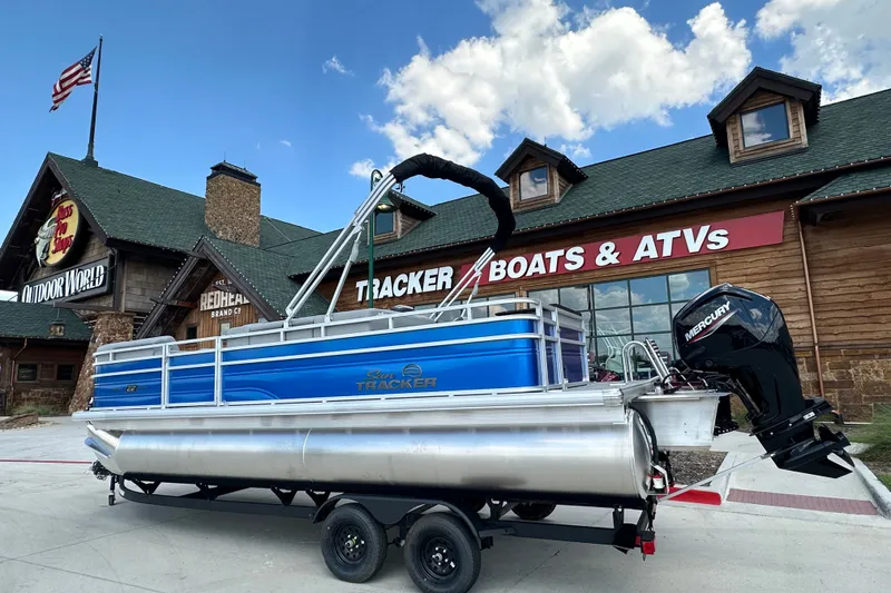 The Image of 2027 Sun Tracker SportFish 22 DLX pontoon boat displayed outside a store with American flag. - 0