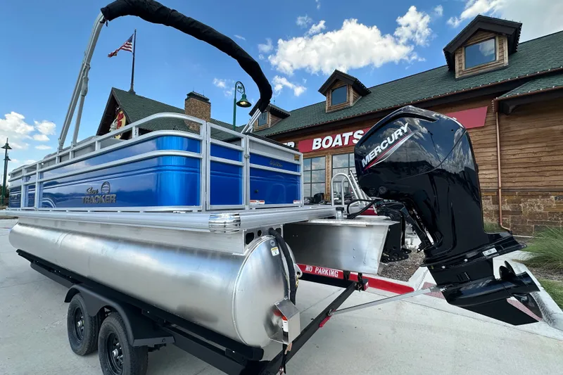Slide: The Image of 2027 Sun Tracker SportFish 22 DLX pontoon boat with Mercury engine, parked outside a boat store. - 14