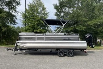 The Image of 2027 Sun Tracker SportFish 22 DLX pontoon boat on trailer, parked outdoors. - 0