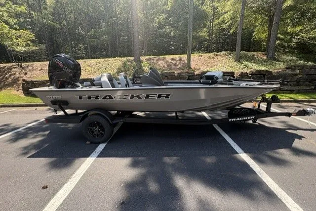 The Image of 2027 Tracker Pro Team 195 boat on trailer in a wooded parking area. - 0