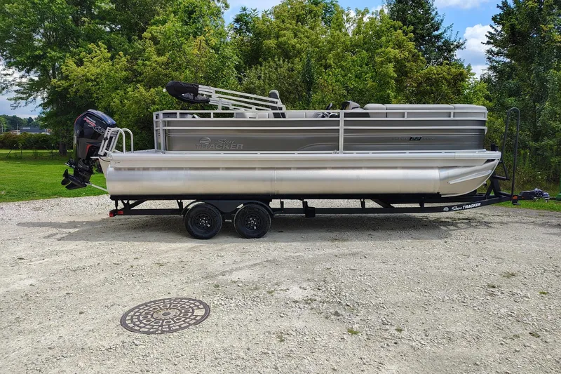 The Image of 2027 Sun Tracker SportFish 22 DLX pontoon boat on trailer, parked outdoors. - 0