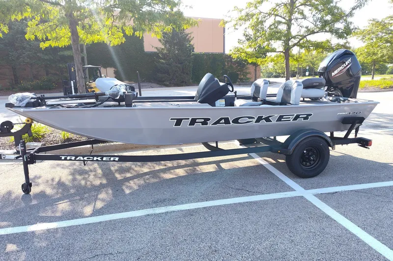 The Image of A gray Tracker Pro 170 boat on a trailer in a parking lot, surrounded by trees. - 0