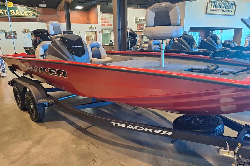 The Image of 2027 Tracker Pro Team 195 boat on display in showroom, featuring red hull and trailer. - 0