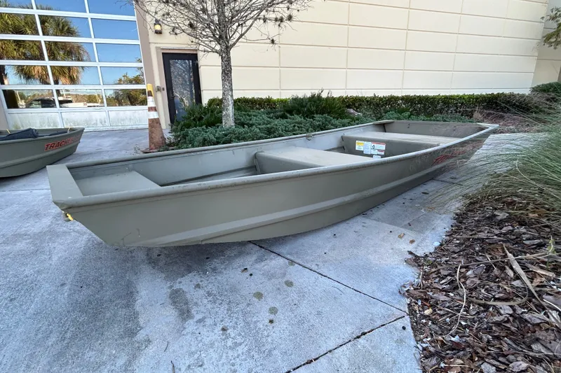 The Image of 2027 Tracker Grizzly 12 Jon boat on concrete near building and greenery. - 0