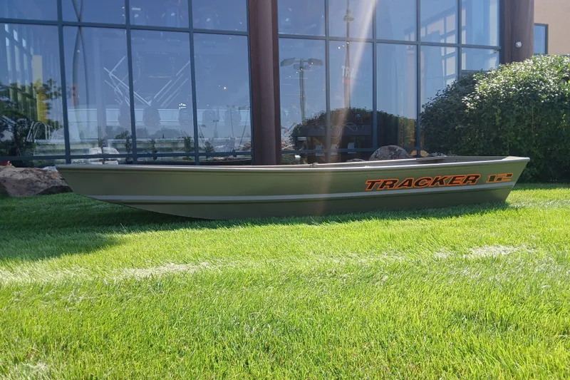 The Image of 2027 Tracker Grizzly 12 Jon boat displayed on grass outside a glass building. - 0