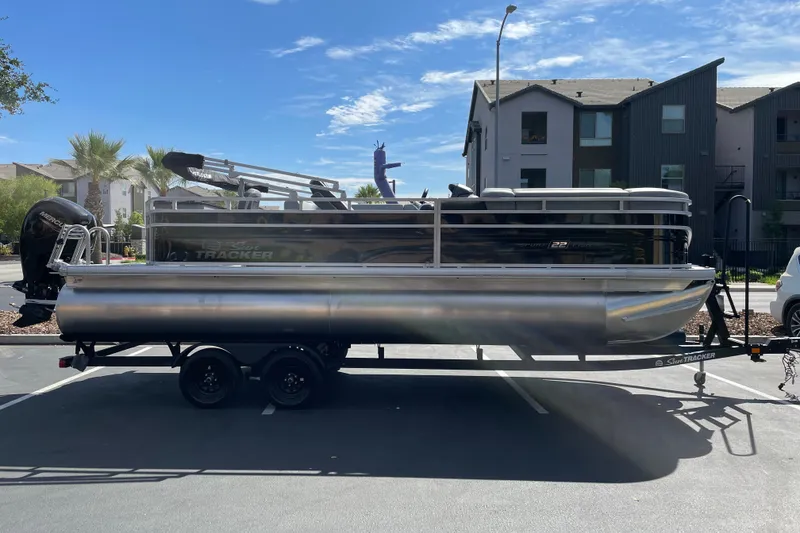 The Image of 2027 Sun Tracker SportFish 22 DLX pontoon boat on trailer in parking lot. - 0