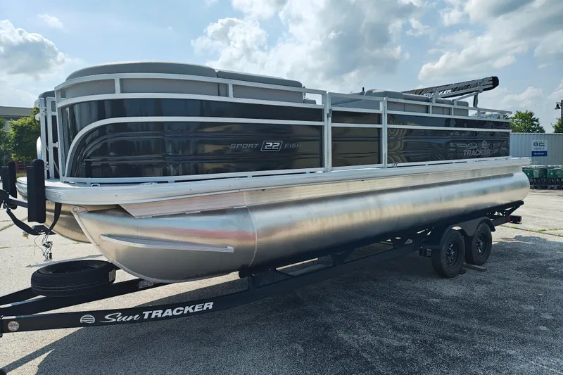 The Image of 2027 Sun Tracker SportFish 22 DLX pontoon boat on trailer under a cloudy sky. - 0