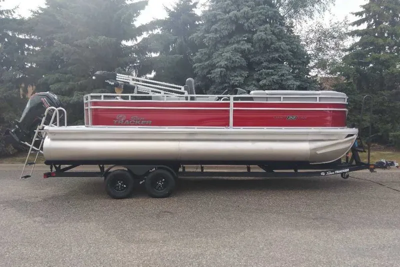 The Image of 2027 Sun Tracker SportFish 22 DLX pontoon boat on trailer, parked outdoors. - 0