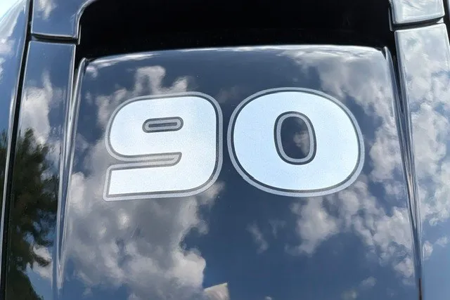 Slide: The Image of Tracker Grizzly 1860 CC 2027 boat engine cover with '90' decal, reflecting cloudy sky. - 14