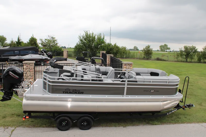 The Image of 2027 Sun Tracker SportFish 22 DLX pontoon boat on trailer, parked on grass. - 0