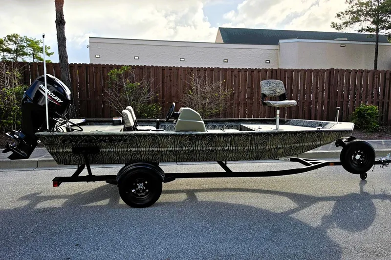 The Image of 2027 Tracker Grizzly 1754 SC boat on trailer, camo design, parked outdoors. - 0