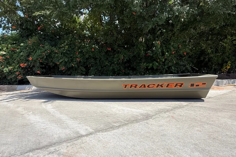 The Image of 2027 Tracker Grizzly 12 Jon boat on pavement, surrounded by lush greenery. - 0