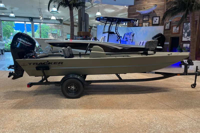 The Image of 2027 Tracker Grizzly 1754 SC boat on trailer in showroom, featuring Mercury outboard motor. - 0