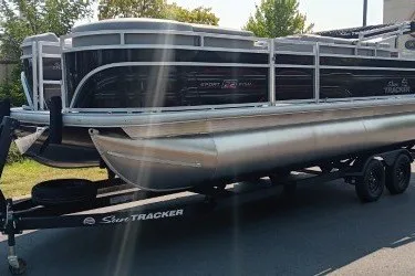 The Image of 2027 Sun Tracker SportFish 22 DLX pontoon boat on trailer, parked outdoors. - 0
