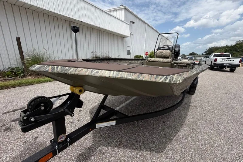 Slide: The Image of 2027 Tracker Grizzly 1860 CC boat on trailer, parked outdoors near a white building. - 67