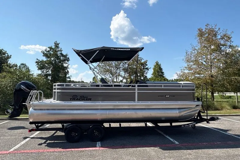 The Image of 2027 Sun Tracker SportFish 22 DLX pontoon boat on trailer, parked outdoors. - 0