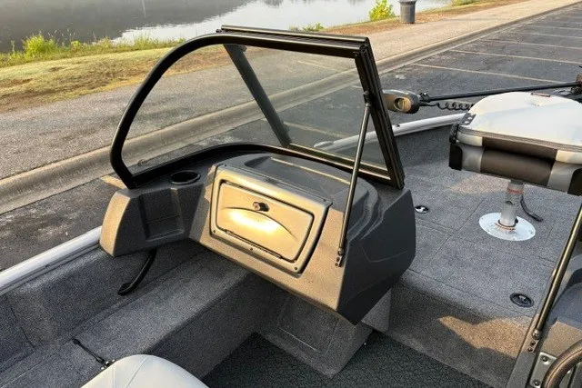 Slide: The Image of 2027 Tracker Pro Guide V-16 WT boat interior with windshield and seating, parked by a lake. - 17