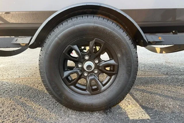 Slide: The Image of 2027 Tracker Pro Guide V-16 WT trailer wheel with black alloy rim on asphalt. - 28