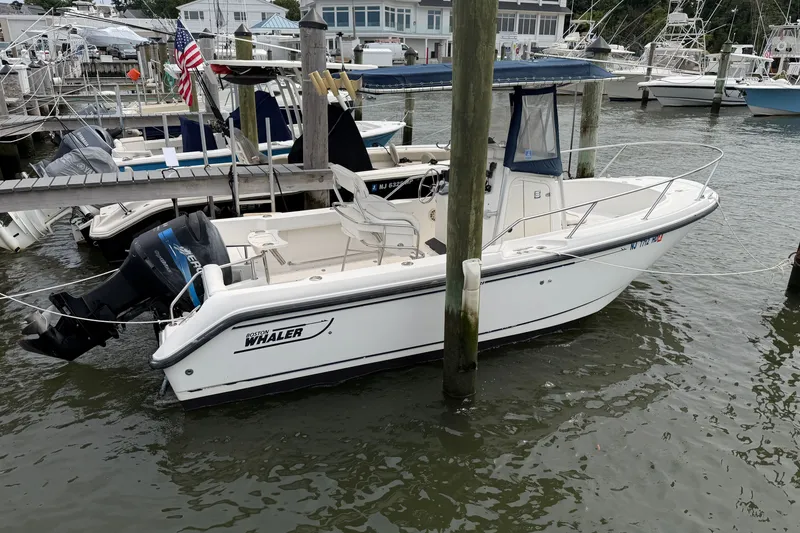 The Image of 2002 Boston Whaler 210 Outrage boat docked at marina, featuring outboard motor. - 2