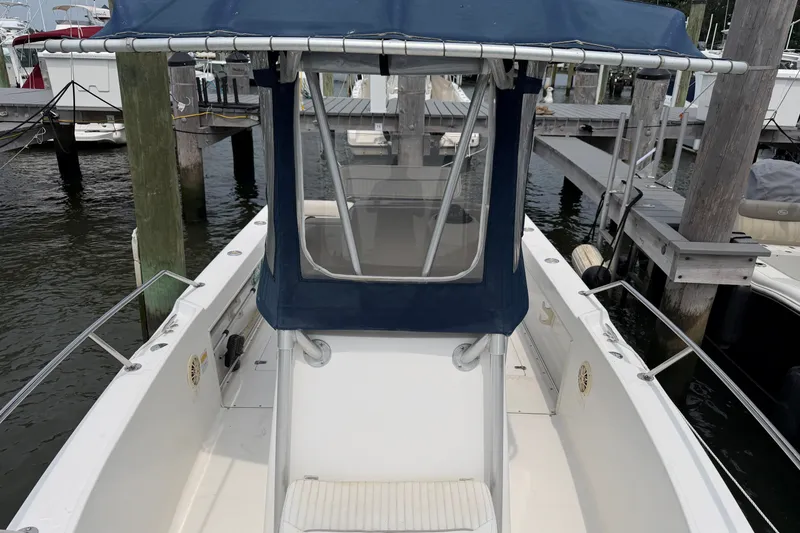 Slide: The Image of 2002 Boston Whaler 210 Outrage boat docked, featuring a blue canopy and spacious deck. - 18