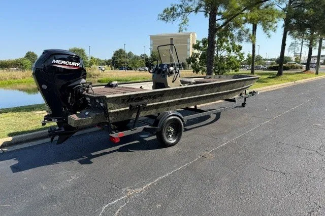 The Image of 2027 Tracker Grizzly 1860 CC boat on trailer, parked outdoors near trees. - 0
