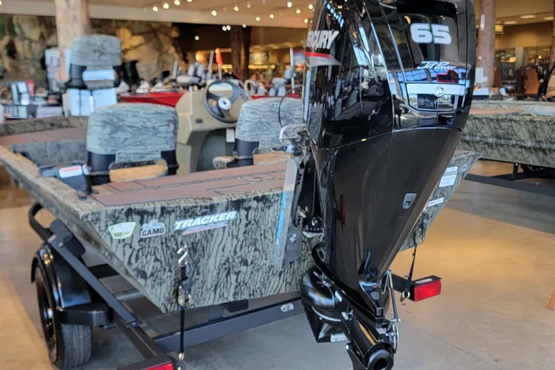 The Image of 2027 Tracker Grizzly 1754 SC boat with camo design and Mercury 65 engine displayed indoors. - 0