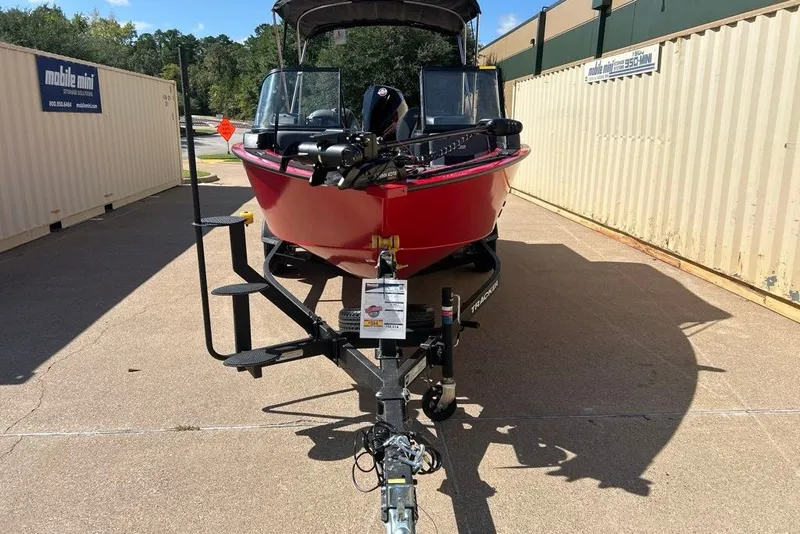 Slide: The Image of Red 2027 Tracker Targa V-18 Combo boat on trailer, parked between storage containers. - 13