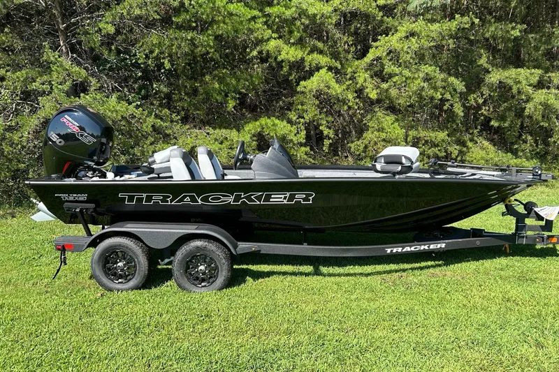The Image of 2027 Tracker Pro Team 195 boat on trailer, parked on grass with forest background. - 0