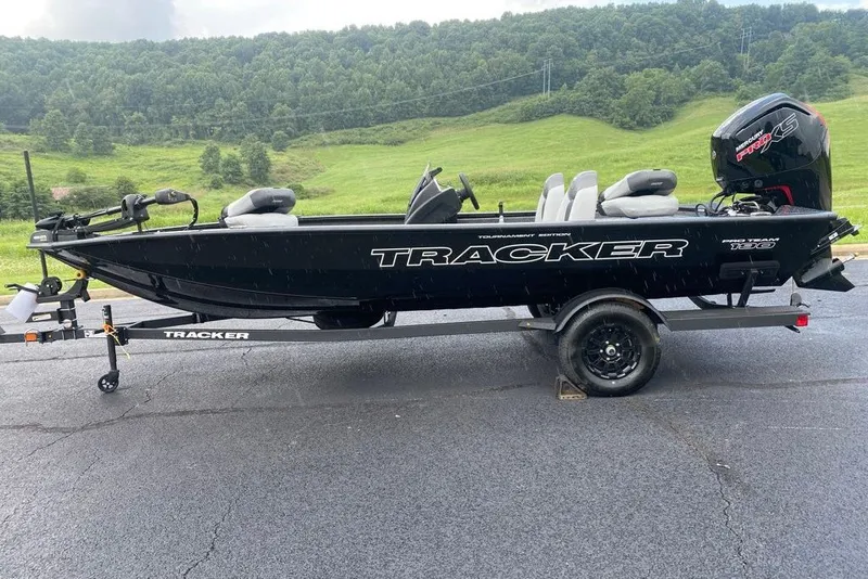The Image of 2027 Tracker Pro Team 190 boat on trailer, parked on asphalt with green hills in background. - 0