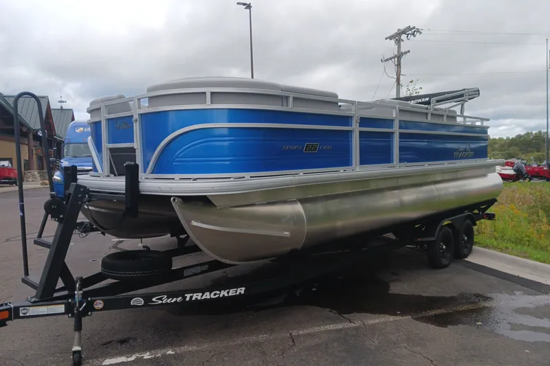 The Image of 2027 Sun Tracker SportFish 22 DLX pontoon boat on trailer, parked outdoors. - 0