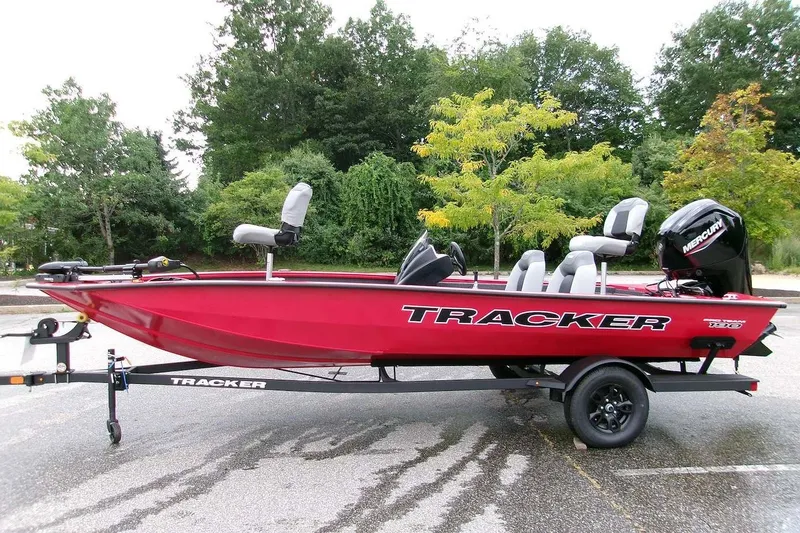 The Image of Red 2027 Tracker Pro Team 190 boat on trailer, parked outdoors with lush greenery background. - 0