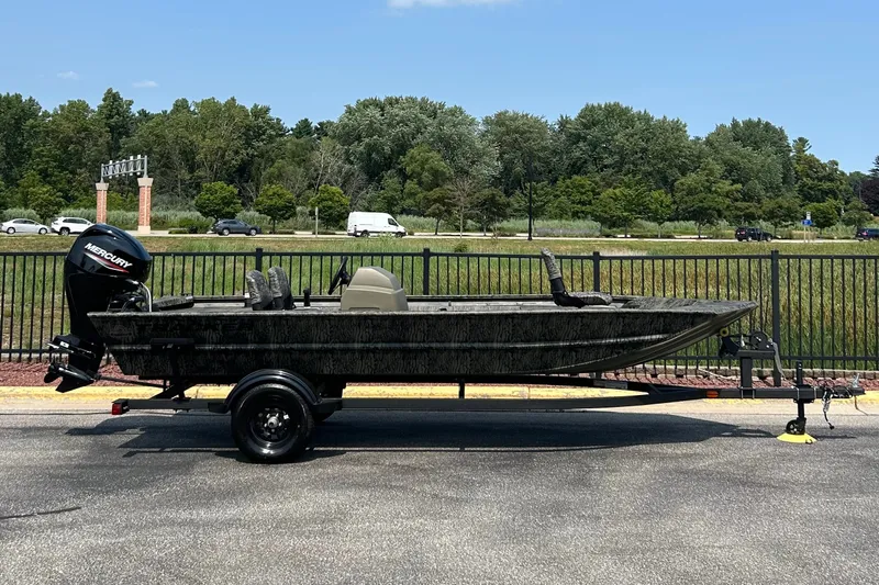The Image of 2027 Tracker Grizzly 1754 SC boat on trailer, parked outdoors with trees in background. - 0