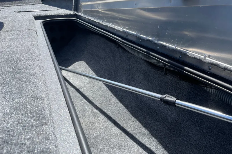 Slide: The Image of 2027 Tracker Pro Team 190 boat storage compartment with carpeted interior and metal support rod. - 21