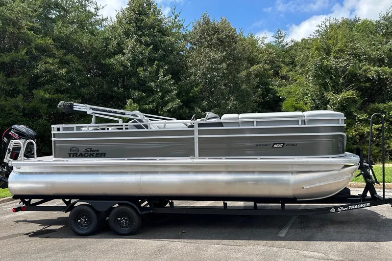 The Image of 2027 Sun Tracker SportFish 22 DLX pontoon boat on trailer, parked outdoors. - 0