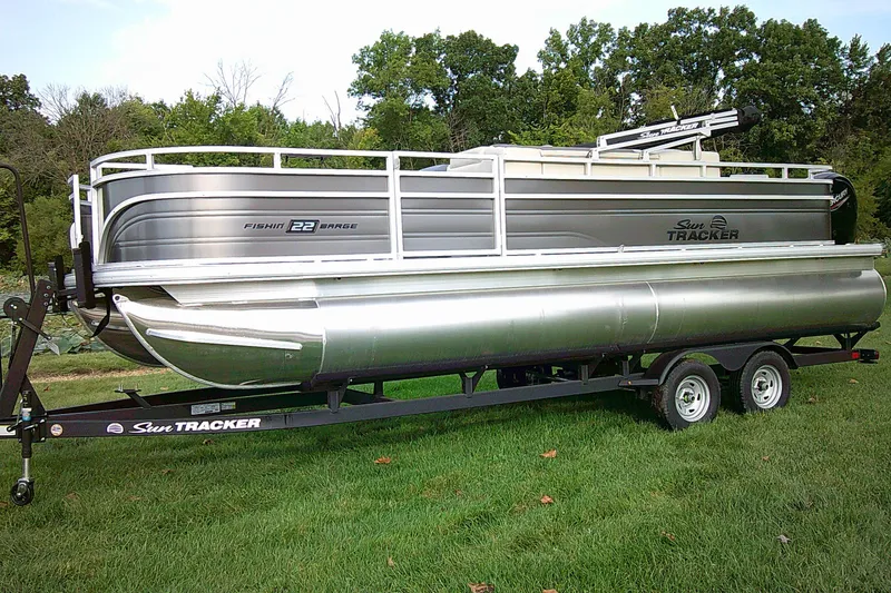 The Image of 2027 Sun Tracker SportFish 22 DLX pontoon boat on trailer, parked on grass. - 0