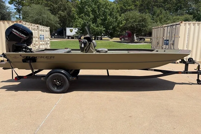 The Image of 2027 Tracker Grizzly 1860 CC boat on trailer, outdoors with trees and containers. - 0