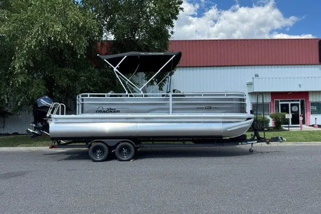The Image of 2027 Sun Tracker SportFish 22 DLX pontoon boat on trailer, parked outdoors. - 0