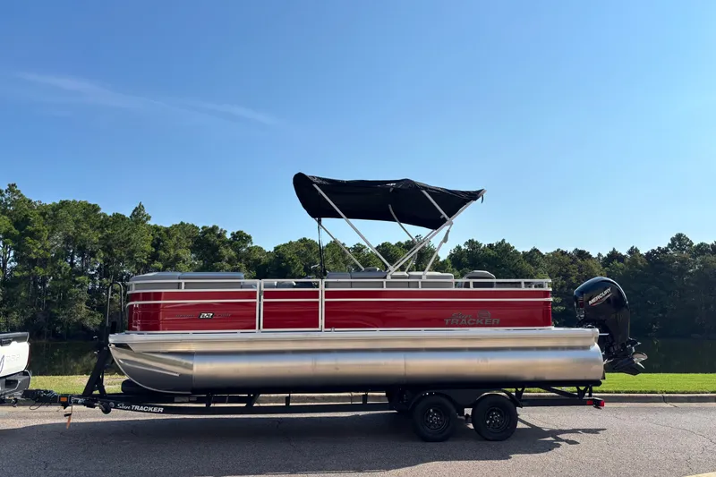 The Image of 2027 Sun Tracker SportFish 22 DLX pontoon boat on trailer, parked near a lake. - 0