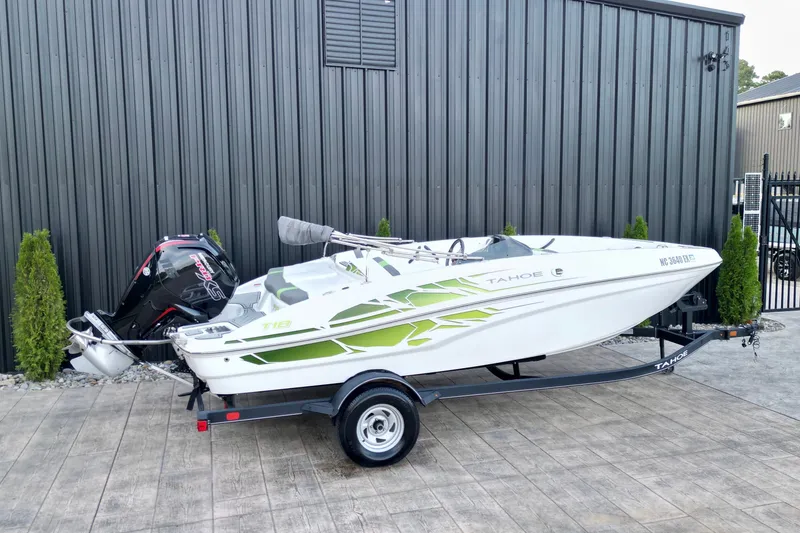Slide: The Image of 2022 Tahoe T18 boat with green accents on a trailer, parked by a metal building. - 16