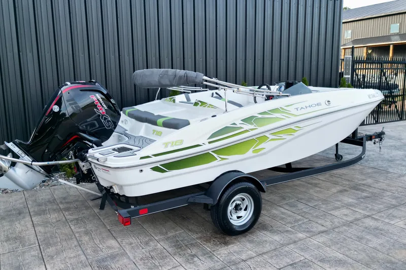 Slide: The Image of 2022 Tahoe T18 boat with green accents on a trailer, parked outdoors. - 2