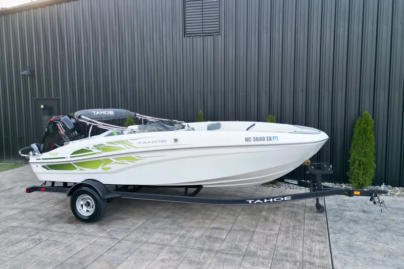 Slide: The Image of 2022 Tahoe T18 boat on trailer, white with green accents, parked by a black building. - 15