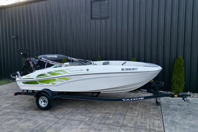 Slide: The Image of 2022 Tahoe T18 boat on trailer, white with green accents, parked by a black building. - 14