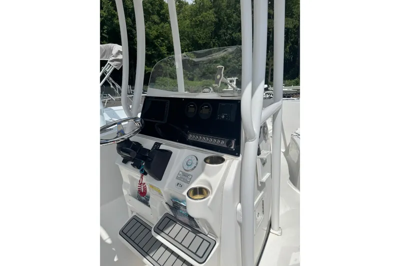 Slide: The Image of 2021 Tidewater 220 LXF boat console with steering wheel and controls, surrounded by lush greenery. - 8