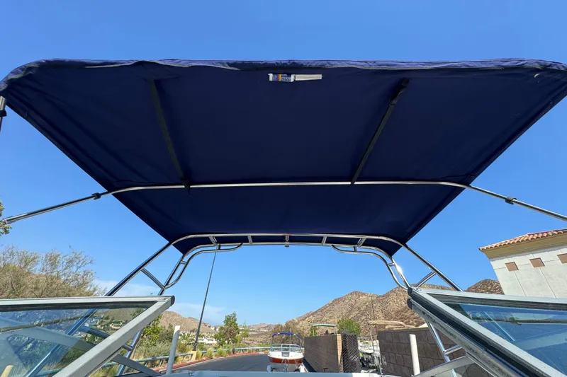 Slide: The Image of 2001 Cobalt 232 boat with blue bimini top against clear sky and scenic background. - 17