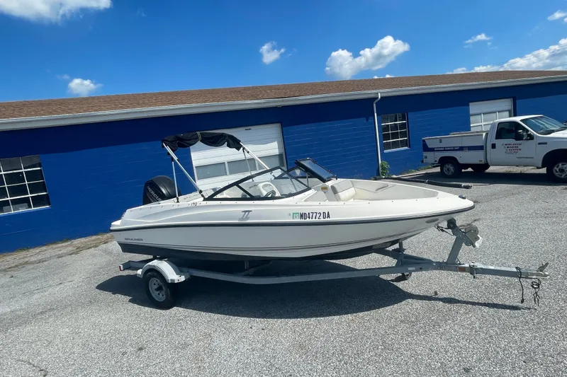 Slide: The Image of 2017 Bayliner 170 Bowrider on trailer, parked near blue building under clear sky. - 13