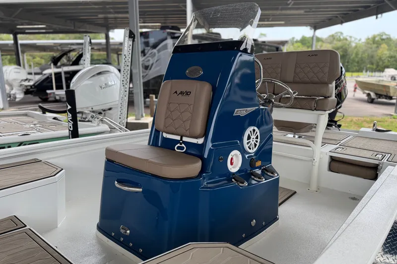 Slide: The Image of 2027 Avid 21 FSX boat interior with blue console and tan seating in a marina. - 15