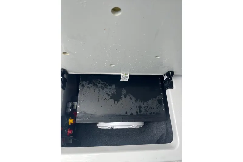 Slide: The Image of 2024 Yamaha Boats AR250 storage compartment with black panel and hinges. - 14
